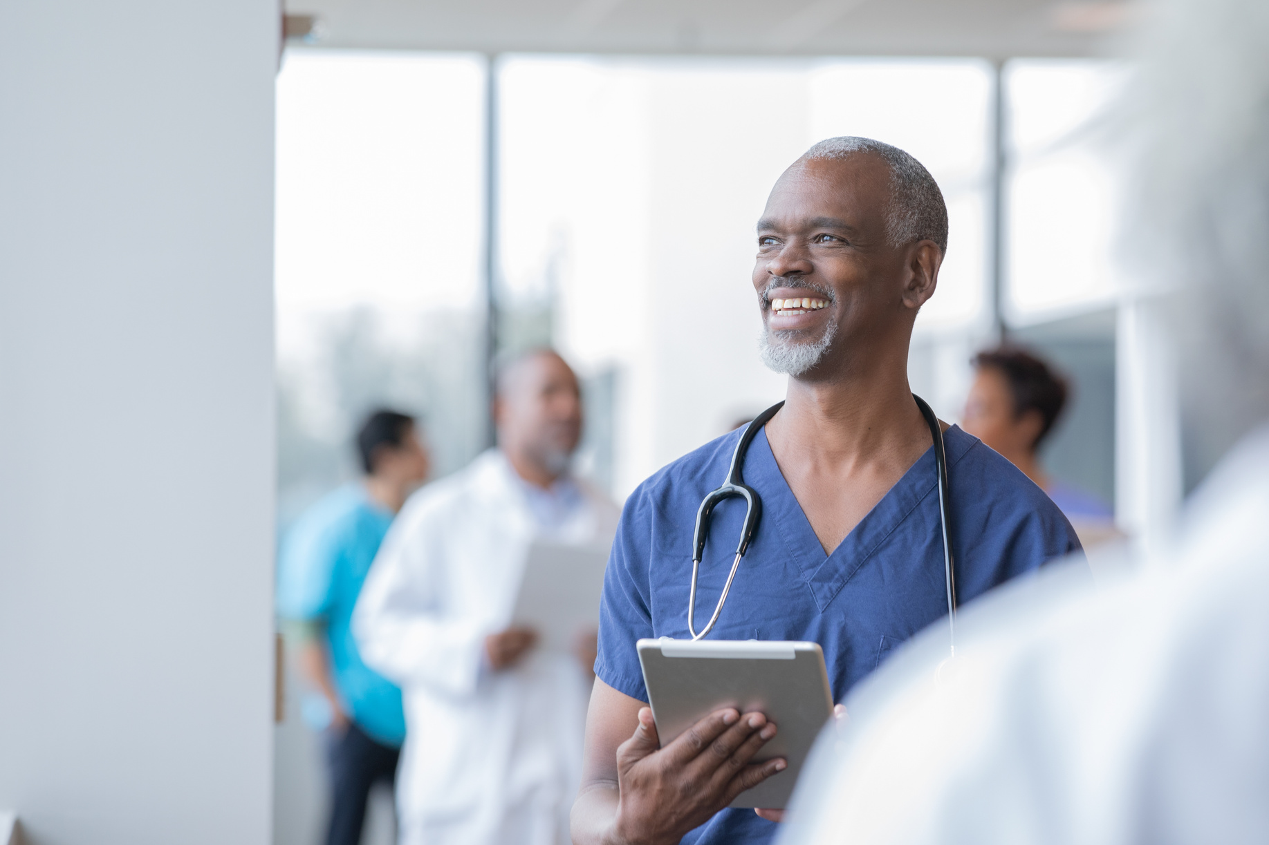 Senior African American doctor holds electronic medical record as he walks through hospital